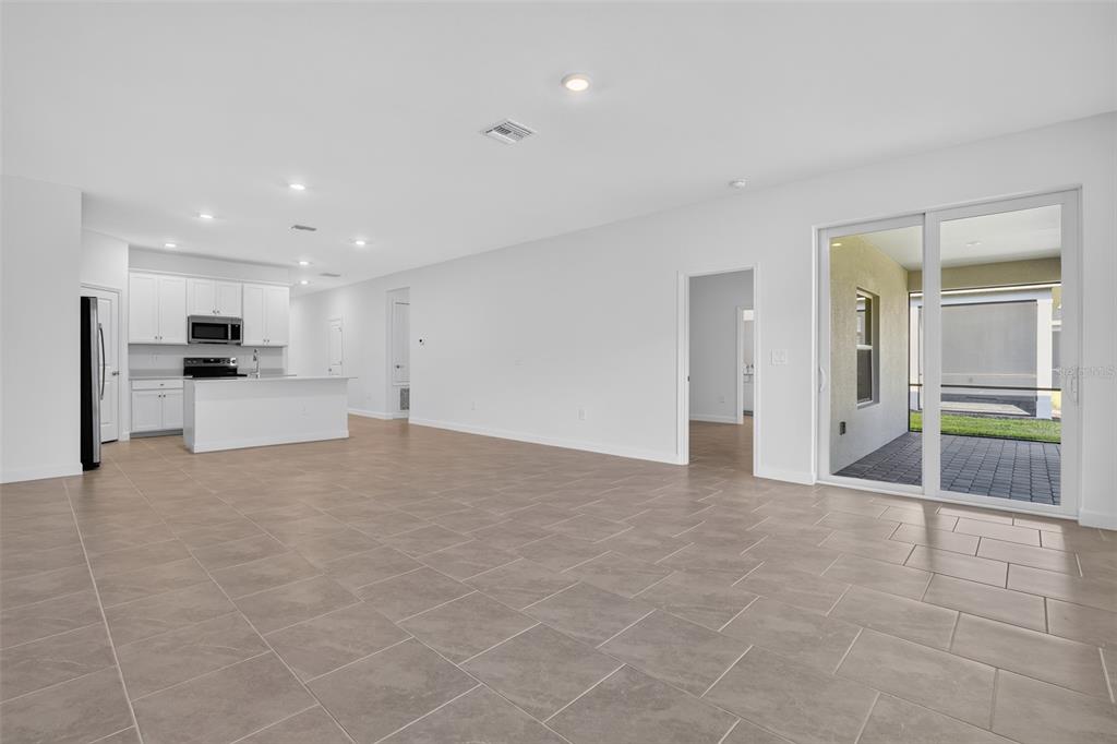 An open-concept living area features light-colored tile flooring, white walls, a kitchen, and sliding doors — 26627 WILGROVE PLACE, PUNTA GORDA, FL