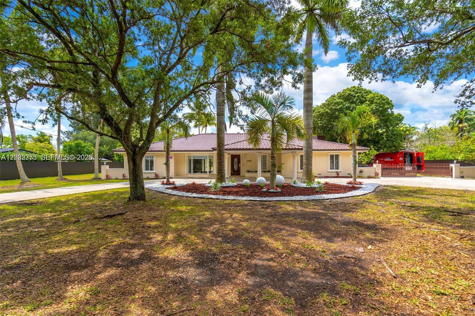 A single-story house with a tiled roof sits behind a circular garden bed with palms — 18370 SW 212th St, Miami FL 33187, MIAMI, FL