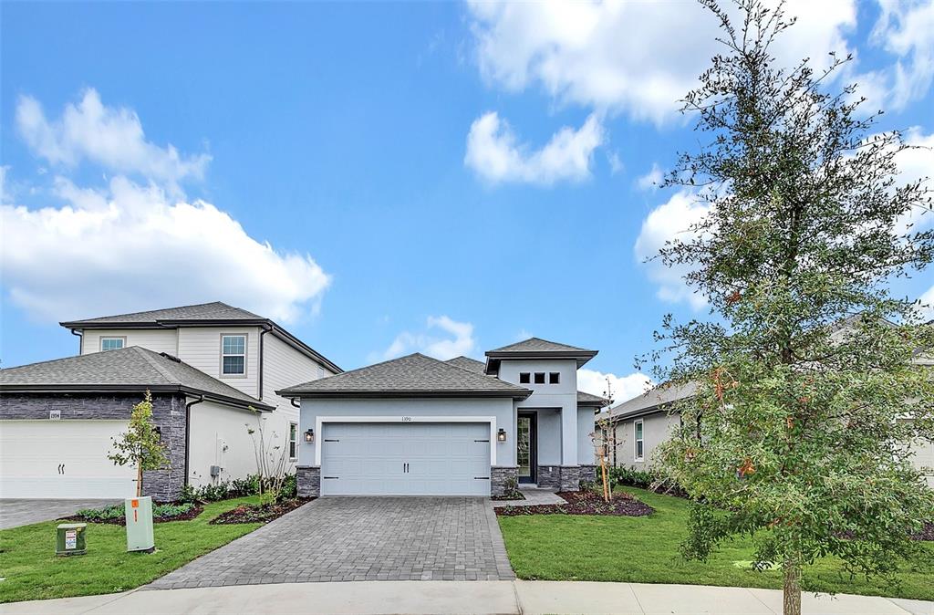 A single-story house with a gray garage, stone accents, and a paved driveway under blue skies — 1390 REMICK COURT, KISSIMMEE, FL