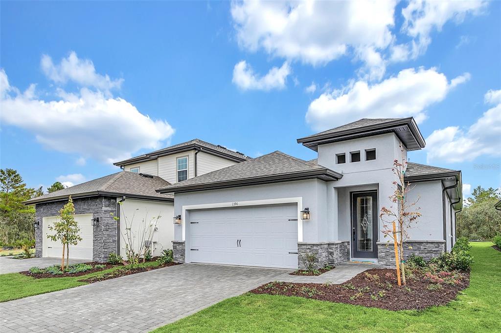 A modern single-story house with a gray stucco exterior, stone accents, and a paved driveway — 1390 REMICK COURT, KISSIMMEE, FL