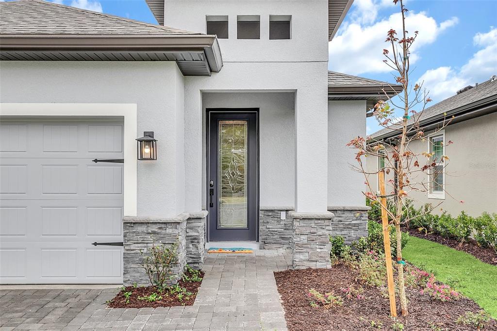 The exterior of a modern house features a gray garage, stone accents, and a glass-paneled door — 1390 REMICK COURT, KISSIMMEE, FL
