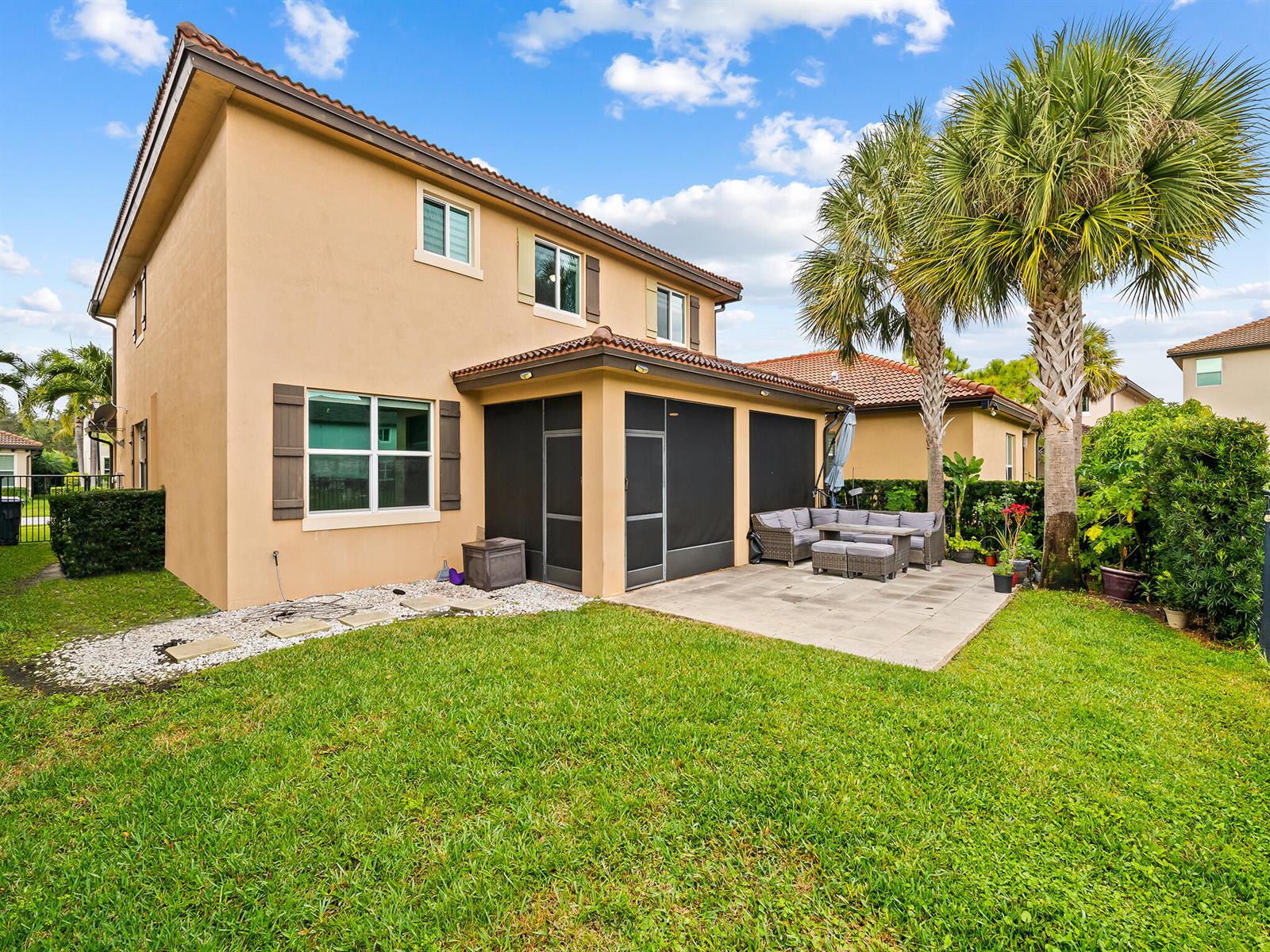 The exterior of a two-story tan house features a screened-in patio and a backyard lawn — 6830 Langdon Way, Lake Worth FL 33463, LAKE WORTH, FL