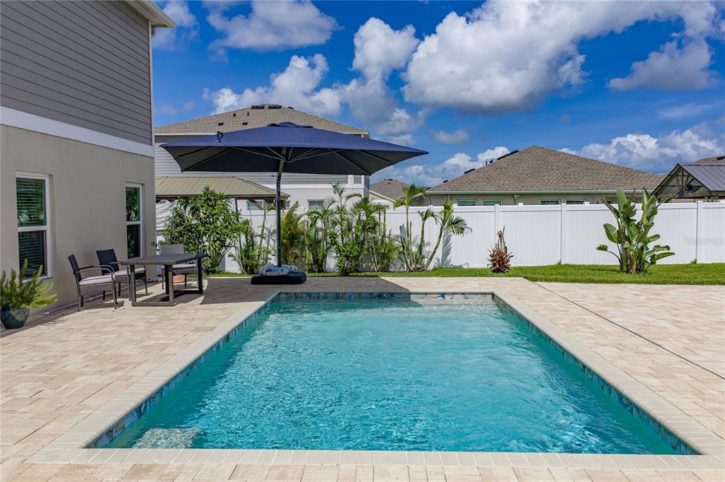 A rectangular swimming pool sits on a paved patio beside a house with an umbrella — 12756 TANNENCREST DRIVE, RIVERVIEW, FL