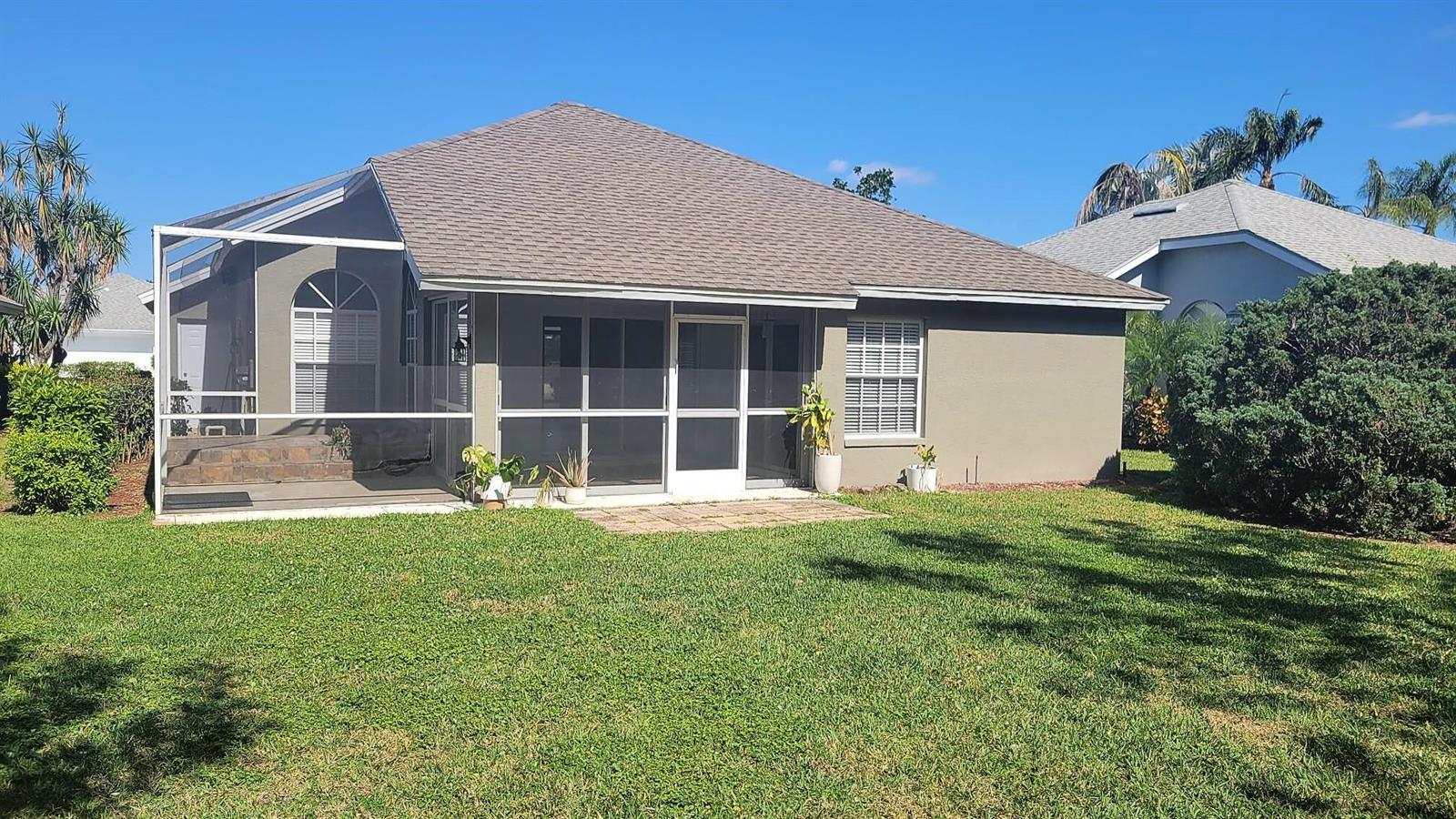 The rear exterior of a single-story house features a screened-in patio and a grassy lawn — 20907 Country Barn Drive, FL 33928, FL