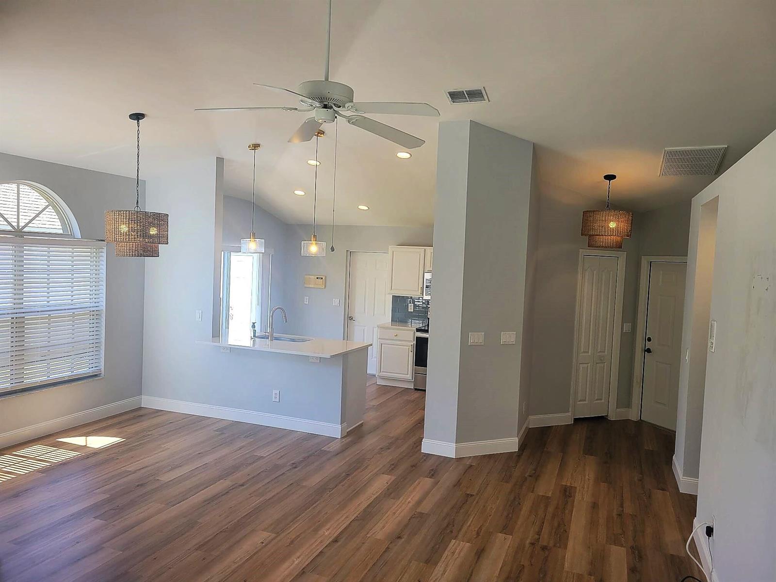 An open-concept living area features wood-look flooring, a kitchen island, and three hanging pendant lights — 20907 Country Barn Drive, FL 33928, FL
