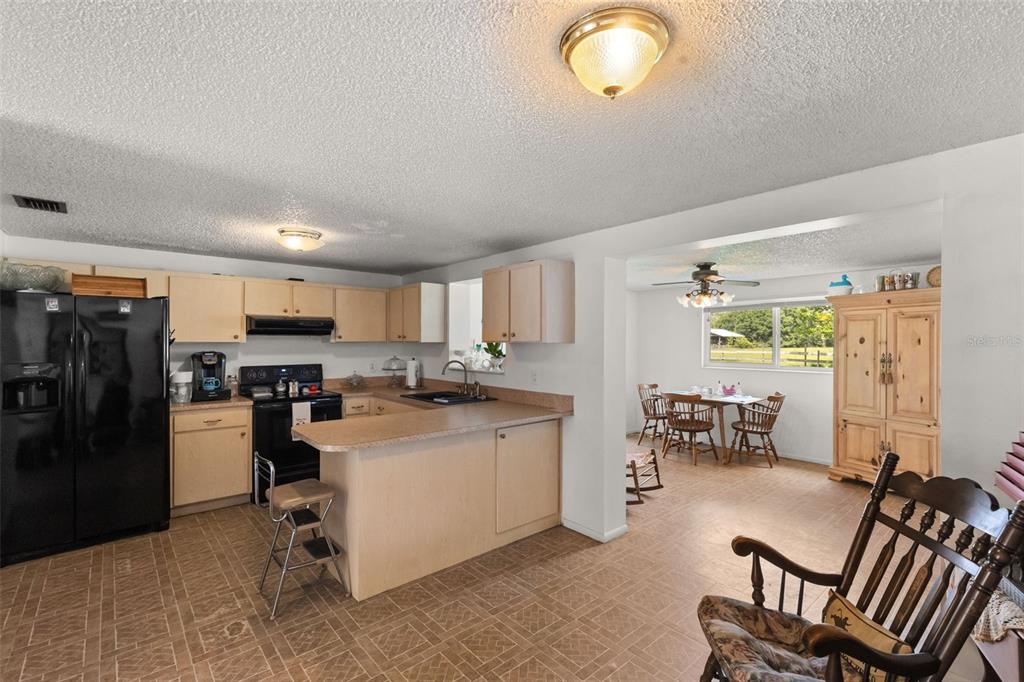A kitchen with light wood cabinets and a breakfast bar opens into a dining area — 12631 HOBSON SIMMONS ROAD, LITHIA, FL
