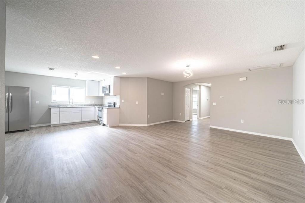 An open-concept kitchen and living area with light gray walls and wood-look flooring — 2025 PEACEFUL PALM STREET, RUSKIN, FL
