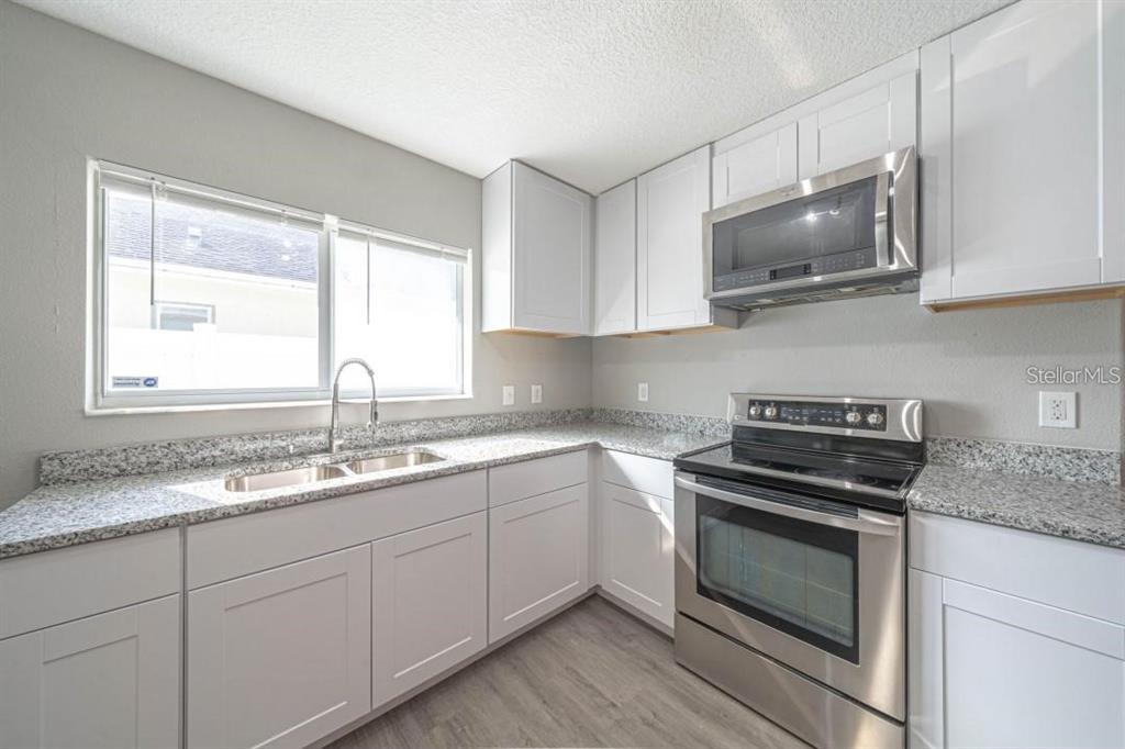A kitchen with white cabinets, stainless steel appliances, and speckled granite countertops — 2025 PEACEFUL PALM STREET, RUSKIN, FL