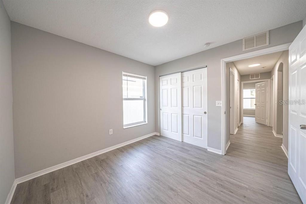 A bedroom with gray walls, light wood-look flooring, a window, and a white sliding closet — 2025 PEACEFUL PALM STREET, RUSKIN, FL