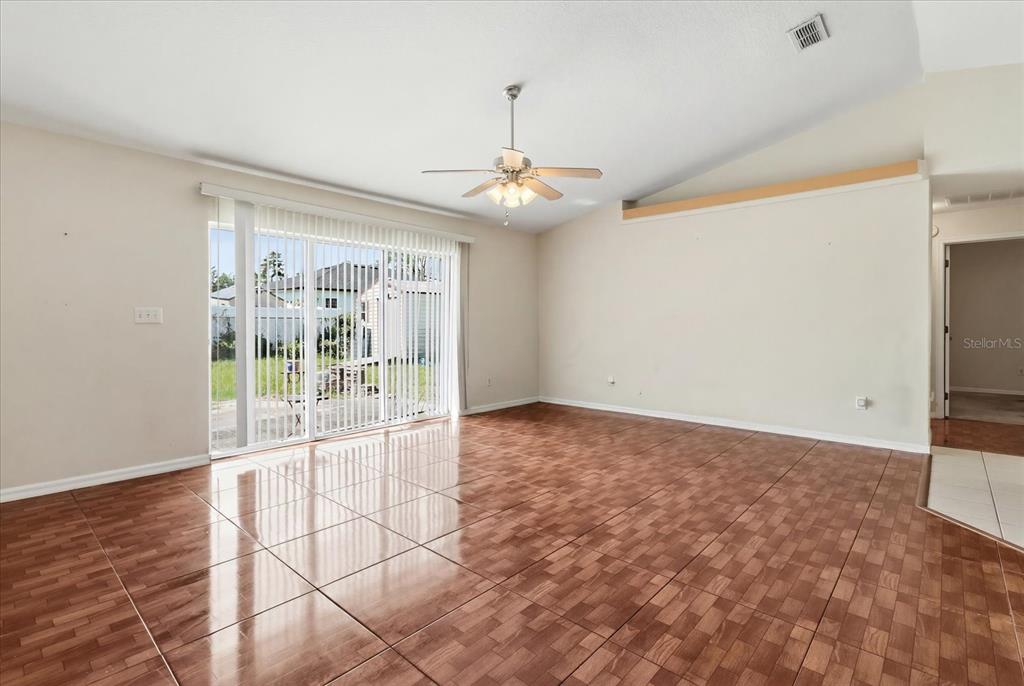 An empty living room features brown tiled flooring, a ceiling fan, and sliding glass doors — 2614 SW 165TH STREET ROAD, OCALA, FL