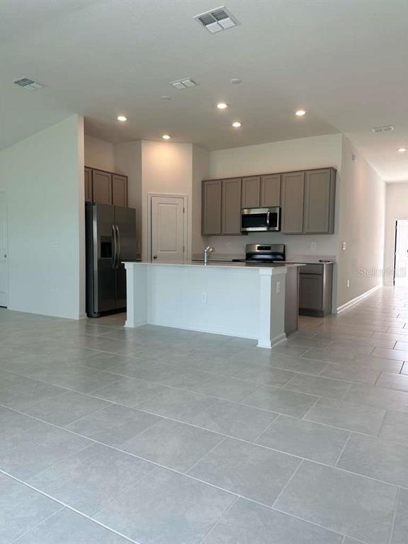 A kitchen features gray cabinets, stainless steel appliances, and a central island on tiled floors — 4816 EDENSBRIDGE LANE, KISSIMMEE, FL