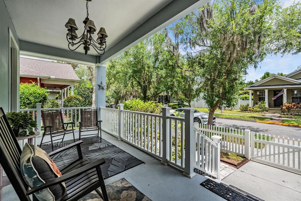 A covered front porch features a chandelier, rocking chairs, and a white picket fence — 10426 MOUNT DORA STREET, NEW PORT RICHEY, FL