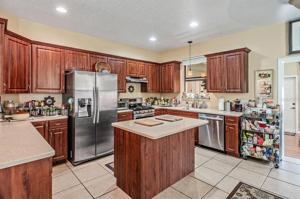 A kitchen with wood cabinets, stainless steel appliances, a center island, and tile flooring — 10426 MOUNT DORA STREET, NEW PORT RICHEY, FL