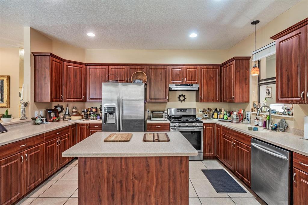 A kitchen with dark wood cabinets, stainless steel appliances, a central island, and tile flooring — 10426 MOUNT DORA STREET, NEW PORT RICHEY, FL