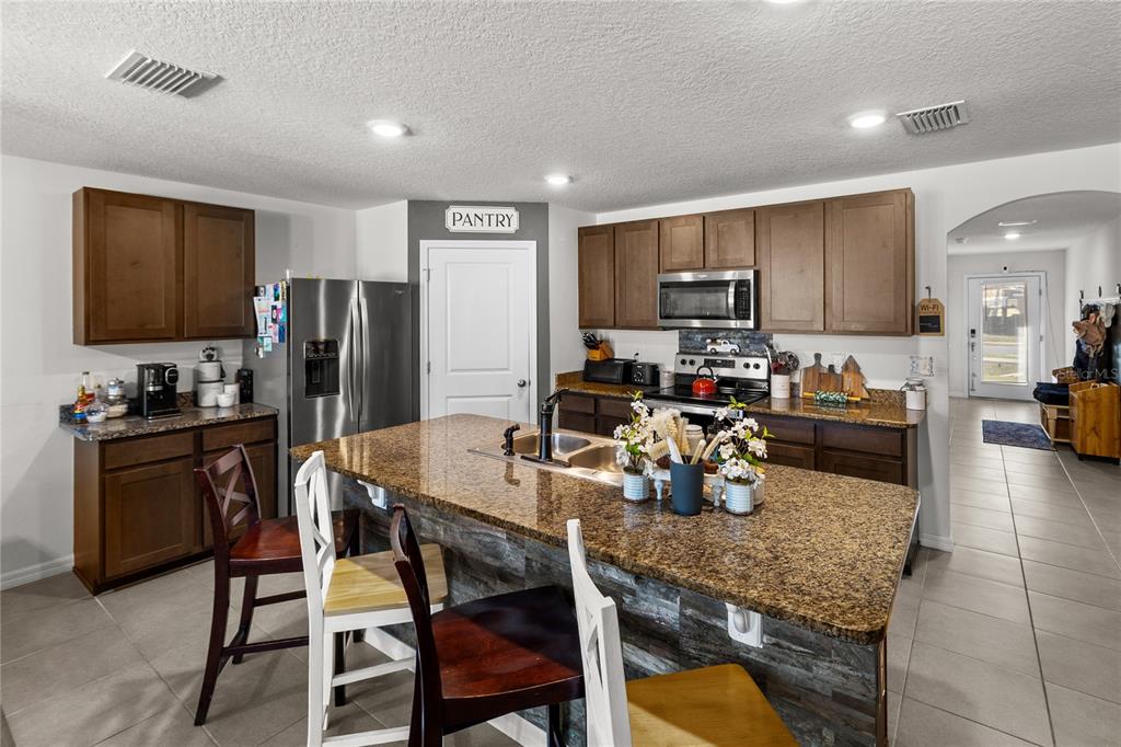 A kitchen features dark wood cabinets, granite countertops, a central island, and stainless steel appliances — 22608 NW 196TH LANE, HIGH SPRINGS, FL