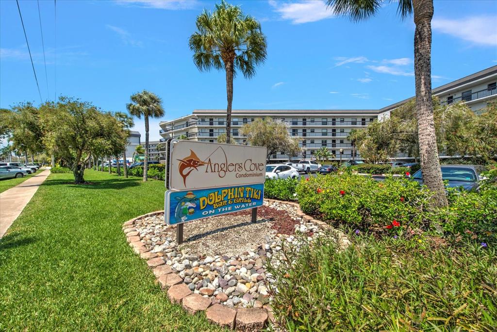 A sign for Anglers Cove Condominium and Dolphin Tiki Bar stands in a landscaped area — 1027 ANGLERS COVE UNIT B502, MARCO ISLAND, FL