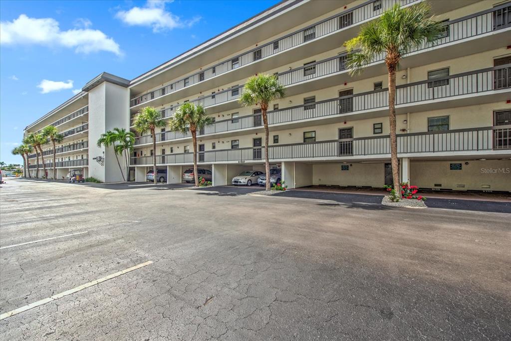 A multi-story apartment building features covered ground-level parking and palm trees in the foreground — 1027 ANGLERS COVE UNIT B502, MARCO ISLAND, FL
