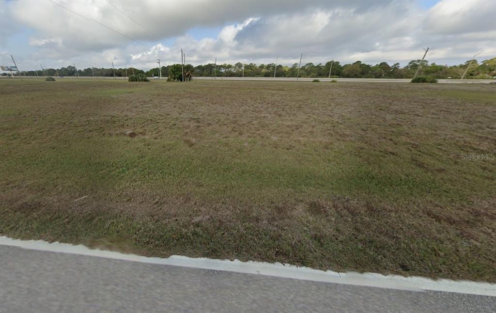 A wide, flat, grassy vacant lot sits adjacent to a paved road under a cloudy sky — 16045 BADALONA DRIVE, PUNTA GORDA, FL