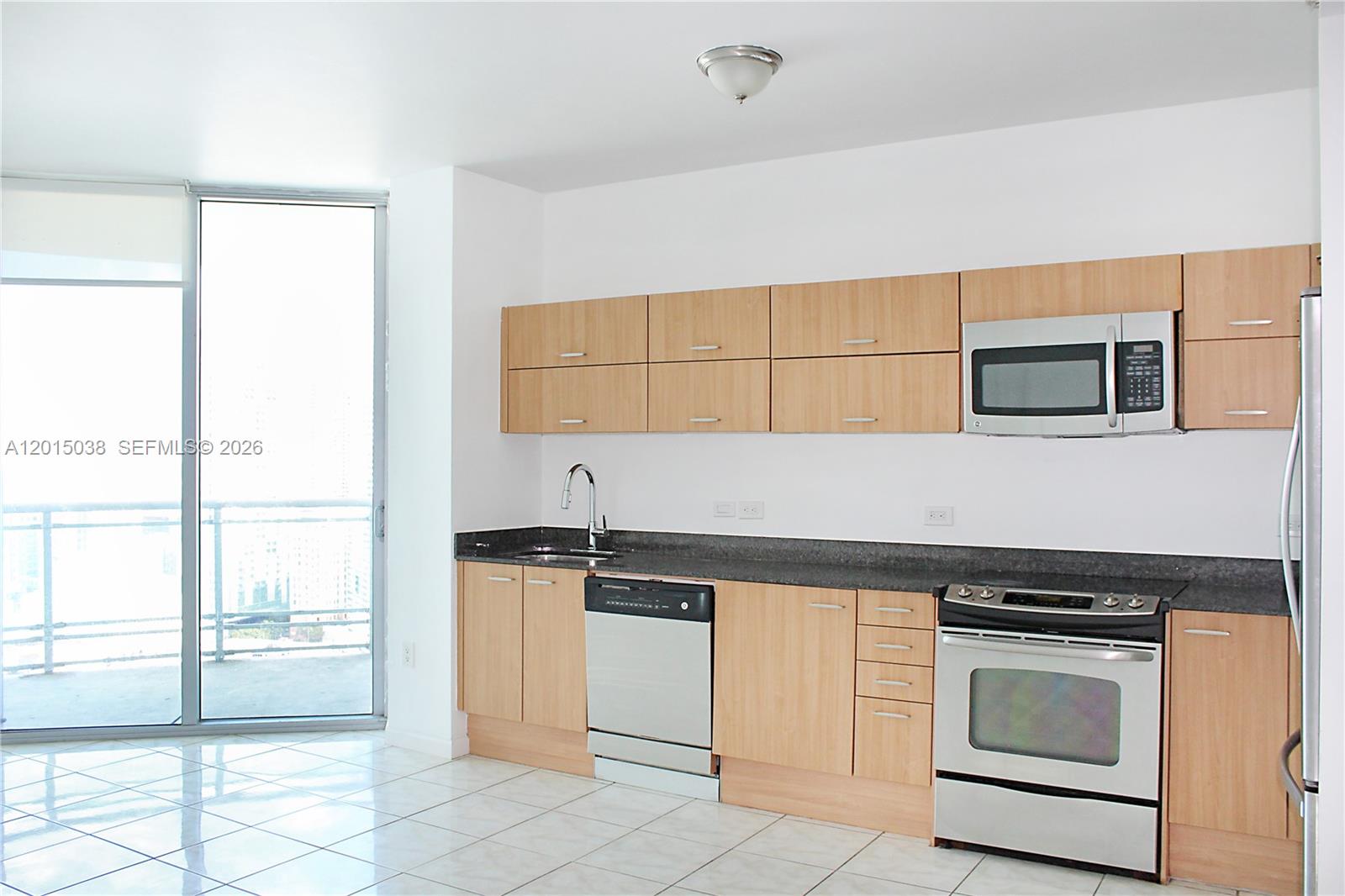 A kitchen features light wood cabinets, stainless steel appliances, dark countertops, and a balcony door — 350 S Miami Ave # 2713, Miami FL 33130, MIAMI, FL