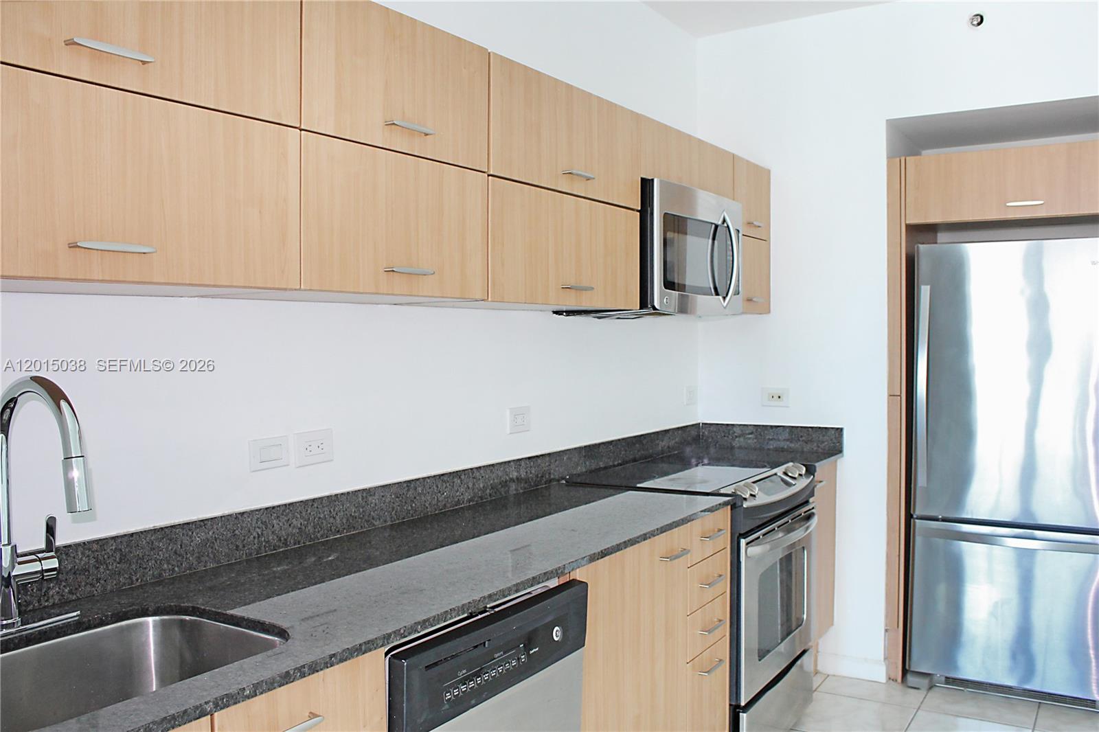 A modern kitchen features light wood cabinets, stainless steel appliances, and dark granite countertops — 350 S Miami Ave # 2713, Miami FL 33130, MIAMI, FL