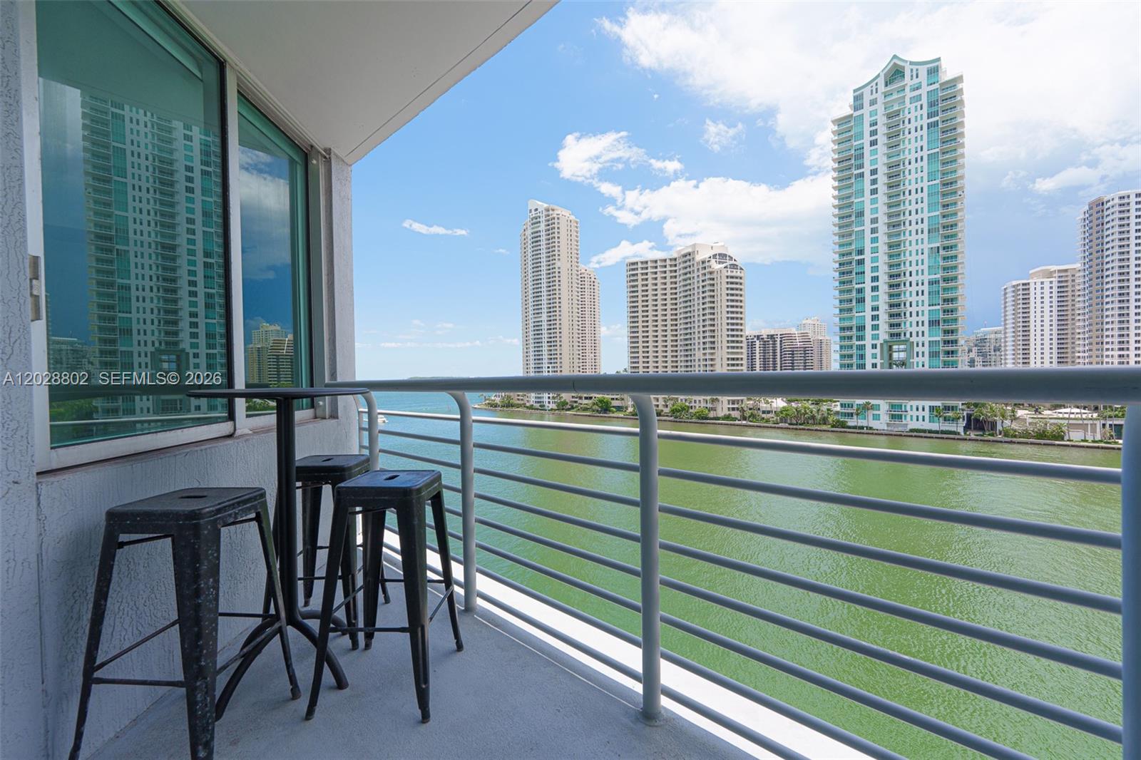 A balcony with a small table and stools overlooks a bay and city skyline — 325 S Biscayne Blvd # 821, Miami FL 33131, MIAMI, FL