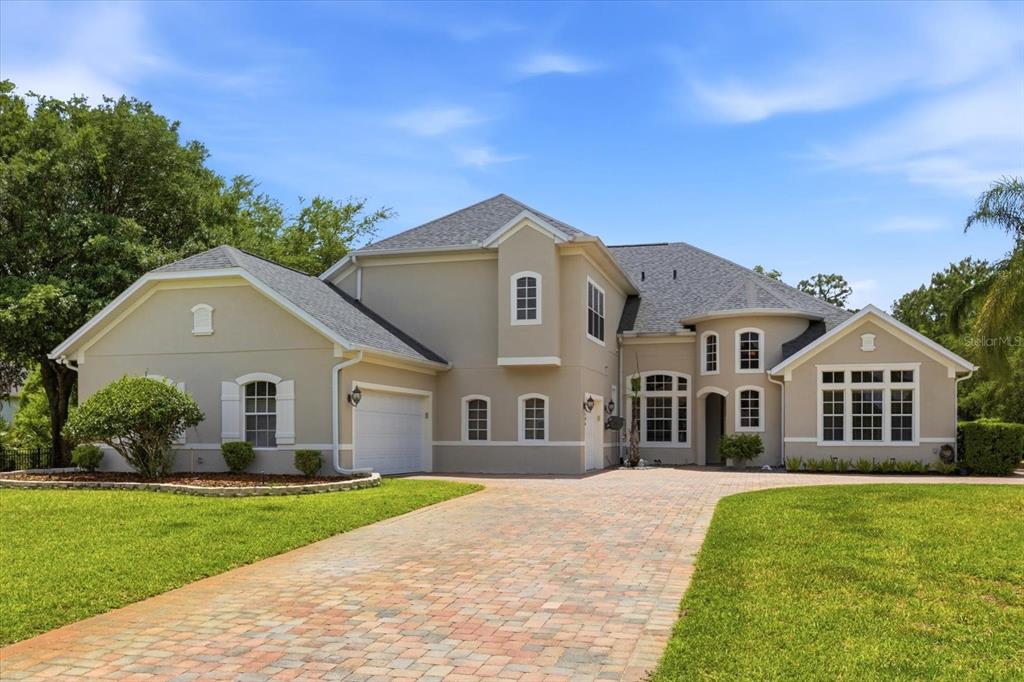 A two-story beige house with a brick paver driveway and a multi-car garage — 14106 OAKWOOD COVE LANE, ORLANDO, FL