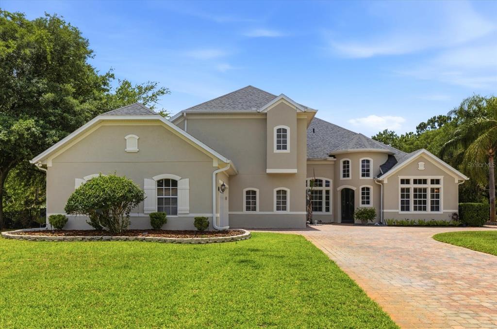 A two-story beige house with a gray shingled roof and a brick paver driveway — 14106 OAKWOOD COVE LANE, ORLANDO, FL