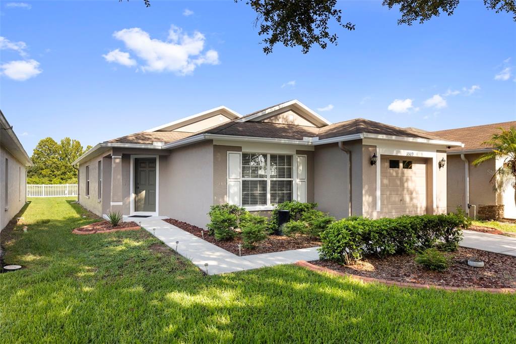 A single-story house with a tan exterior, a front-facing garage, and a landscaped front yard — 10109 LANDPORT WAY, LAND O LAKES, FL