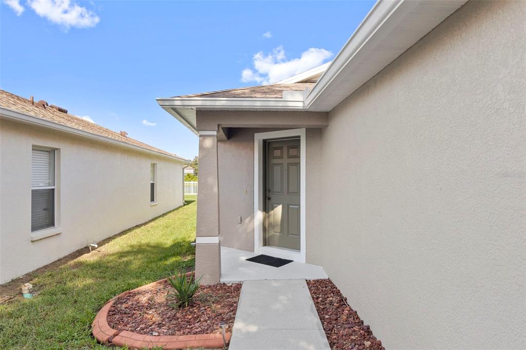 A concrete walkway leads to the front entrance of a beige house with a porch — 10109 LANDPORT WAY, LAND O LAKES, FL