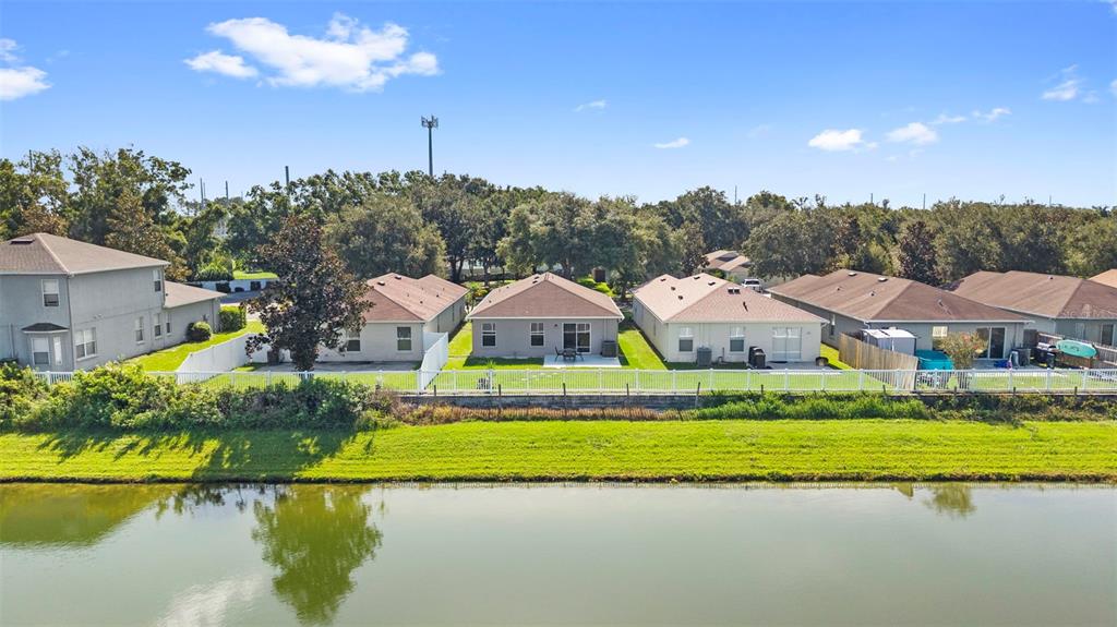 An aerial view shows a row of suburban houses with white fences facing a pond — 10109 LANDPORT WAY, LAND O LAKES, FL