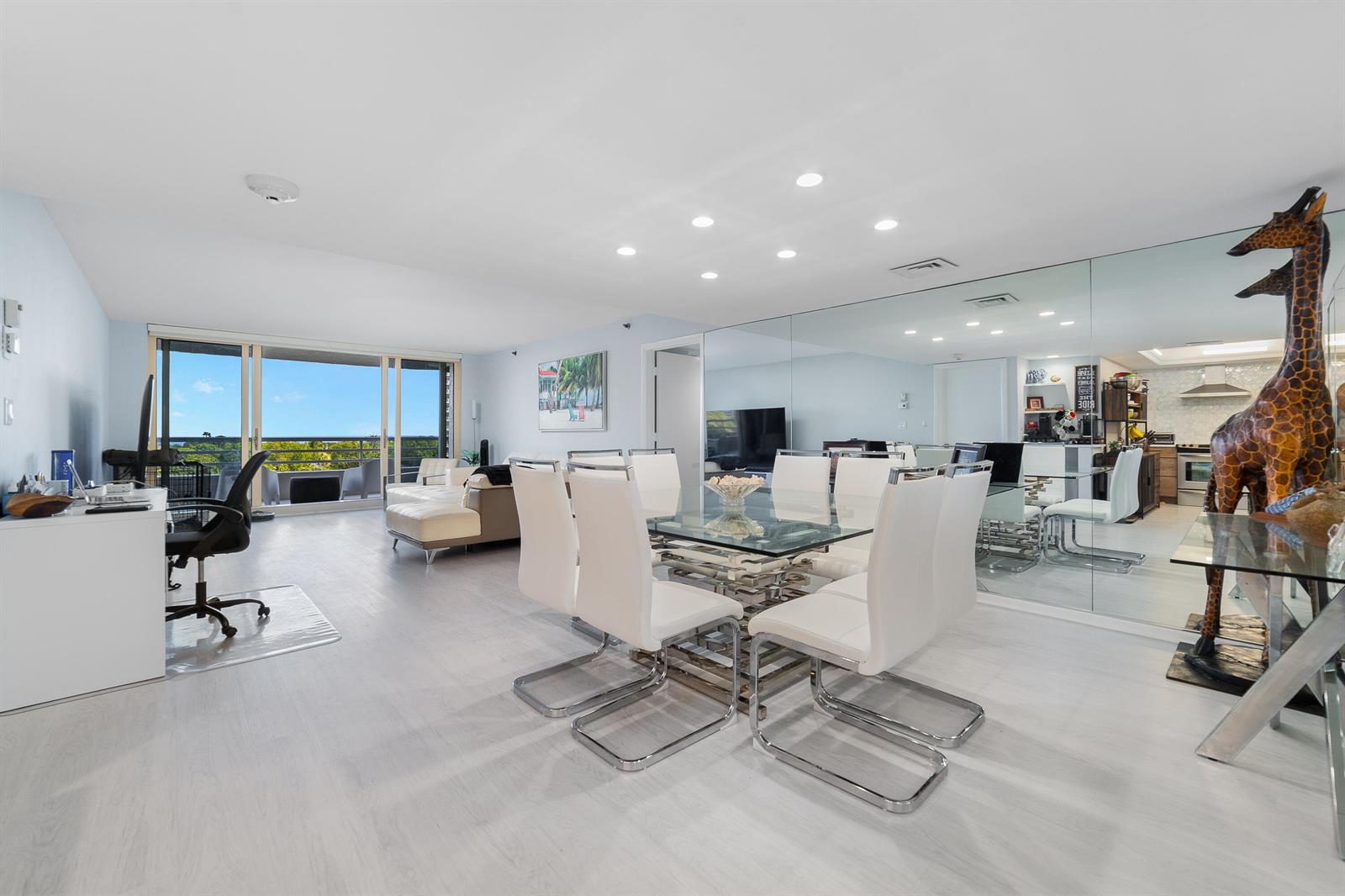 A bright, open-concept living and dining area features white flooring, modern furniture, and mirrored walls — 4101 N Ocean Boulevard # 505, Boca Raton FL 33431, BOCA RATON, FL