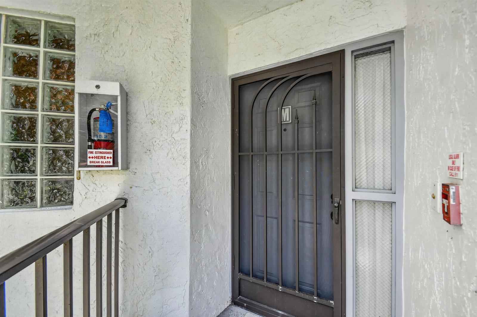 An exterior view of a residential entrance featuring a security door and fire extinguisher — 5394 Firenze Drive, Boynton Beach FL 33437, BOYNTON BEACH, FL