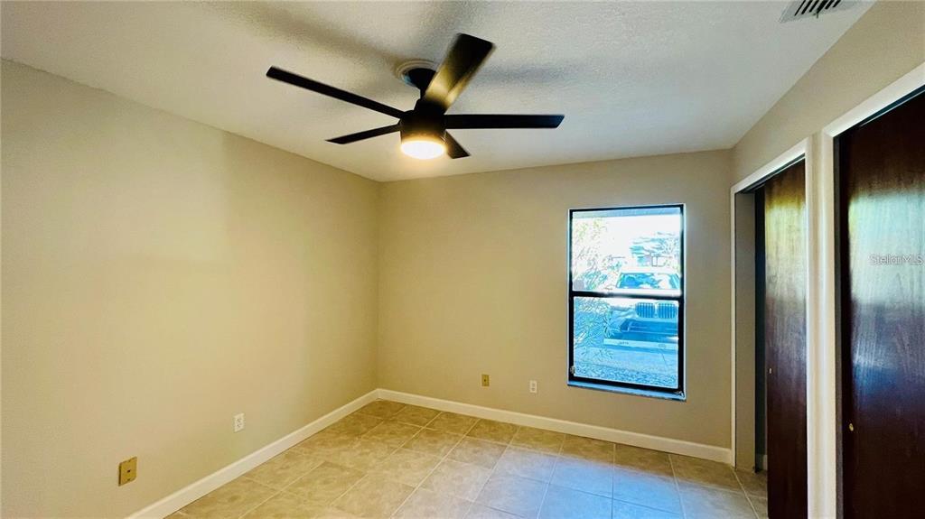 An empty bedroom features beige walls, tile flooring, a ceiling fan, and a window — 2531 KING OAK CIRCLE, ST CLOUD, FL
