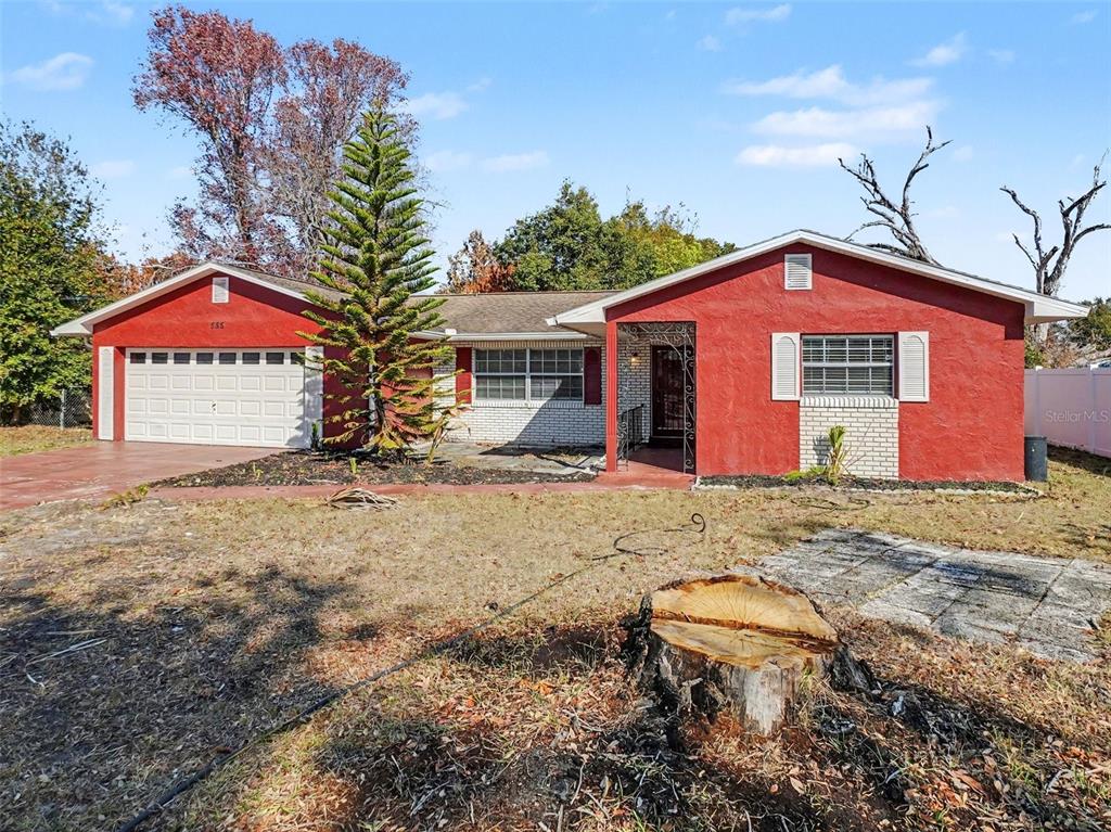 A single-story house with red stucco walls, a white garage, and a large tree stump — 555 THOMAS JEFFERSON WAY, ORLANDO, FL