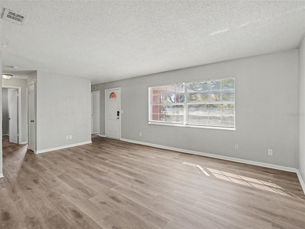 An empty living room features light gray walls, wood-look flooring, and a large window — 555 THOMAS JEFFERSON WAY, ORLANDO, FL
