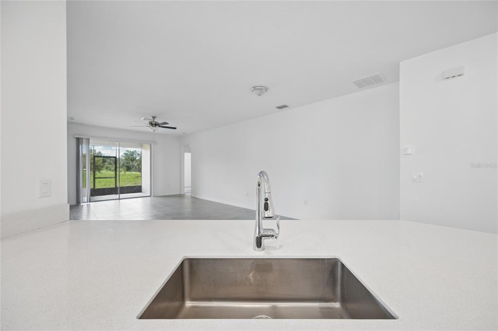 A kitchen sink with a chrome faucet overlooks an open-concept living area with tile floors — 363 LOCH COURT, DAVENPORT, FL