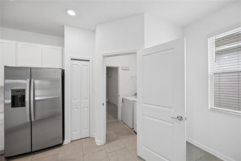 A stainless steel refrigerator stands next to a doorway leading into a laundry room — 363 LOCH COURT, DAVENPORT, FL