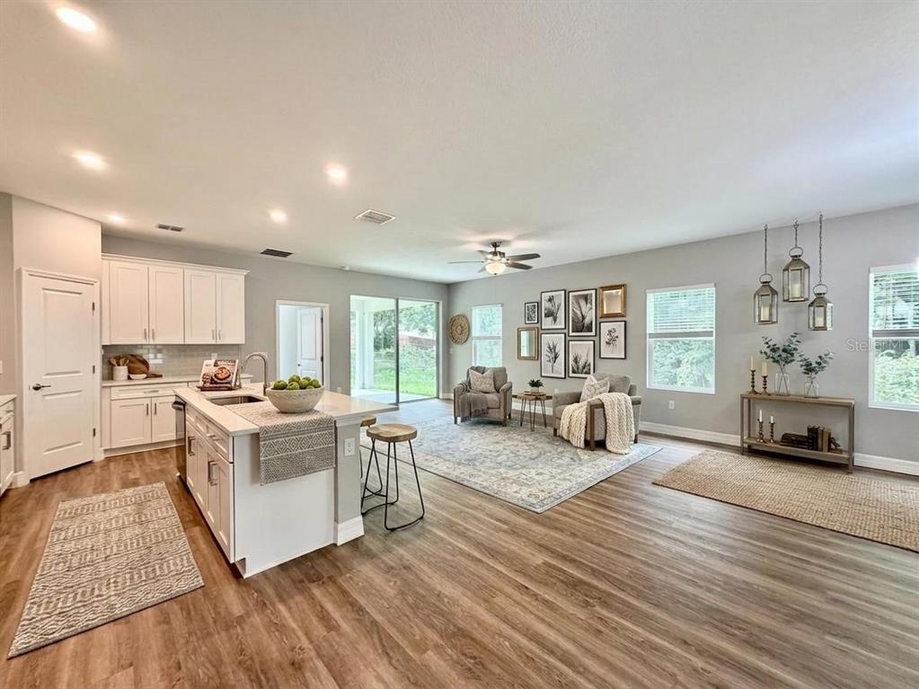 An open-concept kitchen and living area with white cabinetry, wood-look flooring, and a central island — 4198 SW 128TH PLACE, OCALA, FL