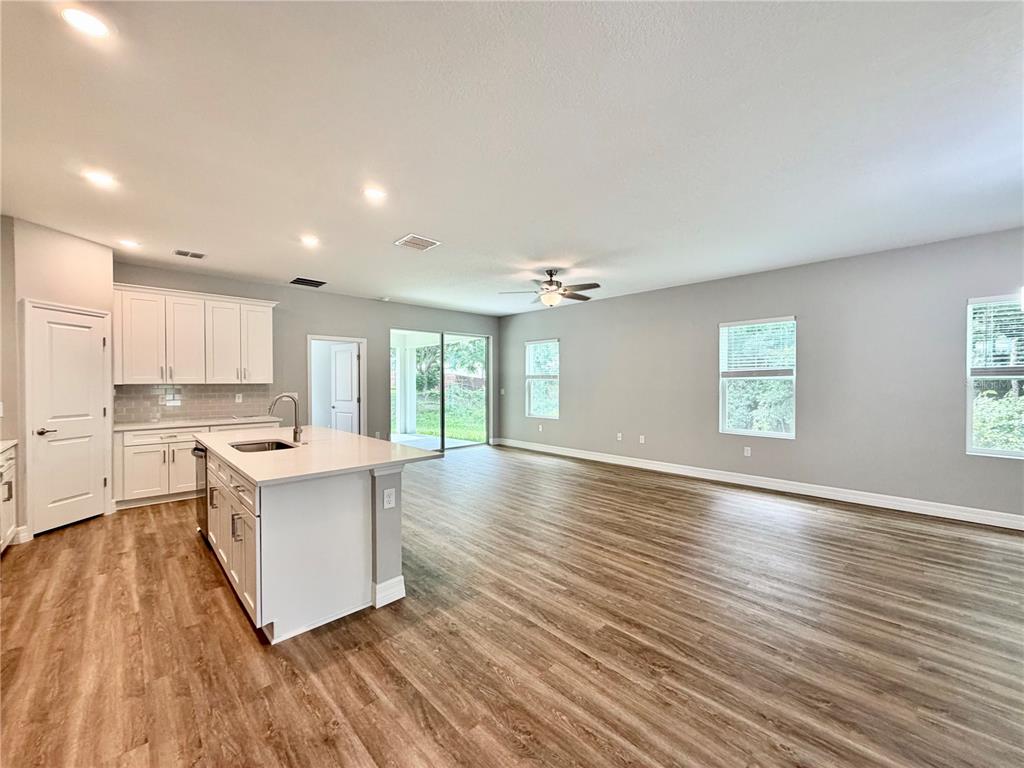 An open-concept kitchen and living area with white cabinets, a center island, and wood-look flooring — 4198 SW 128TH PLACE, OCALA, FL