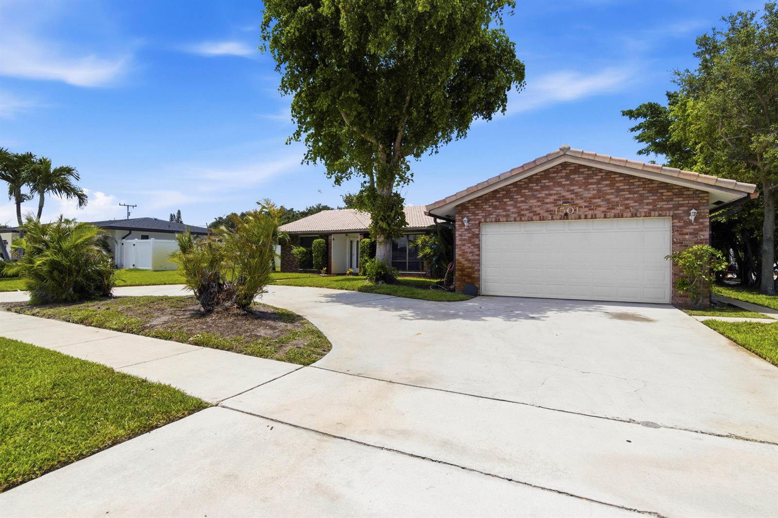 A single-story brick house features a two-car garage, a concrete driveway, and palm trees — 1501 NW 7th Street, Boca Raton FL 33486, BOCA RATON, FL