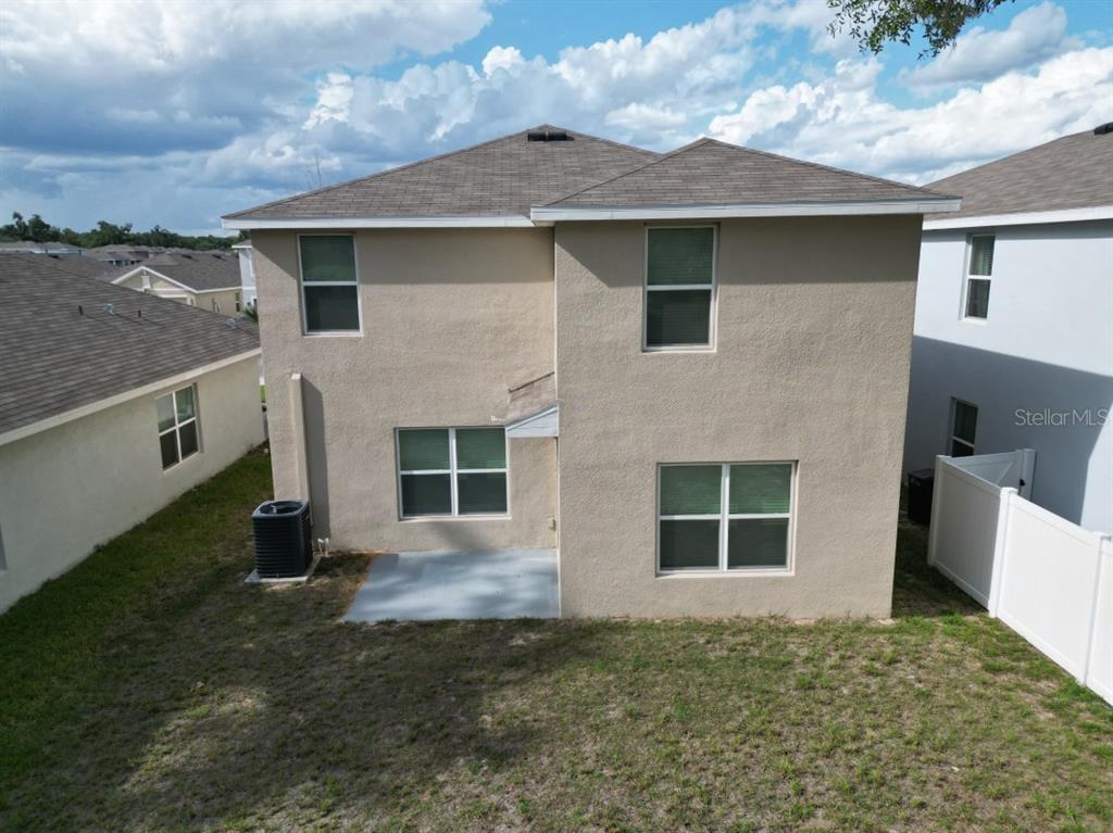 The rear exterior of a two-story stucco house features a concrete patio and yard — 36698 SPANISH ROSE DRIVE, DADE CITY, FL
