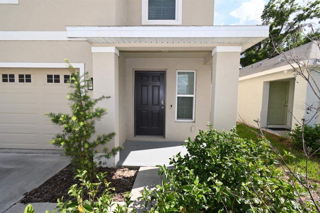 The exterior of a two-story home features a tan stucco facade, a dark front door, and a garage — 36698 SPANISH ROSE DRIVE, DADE CITY, FL