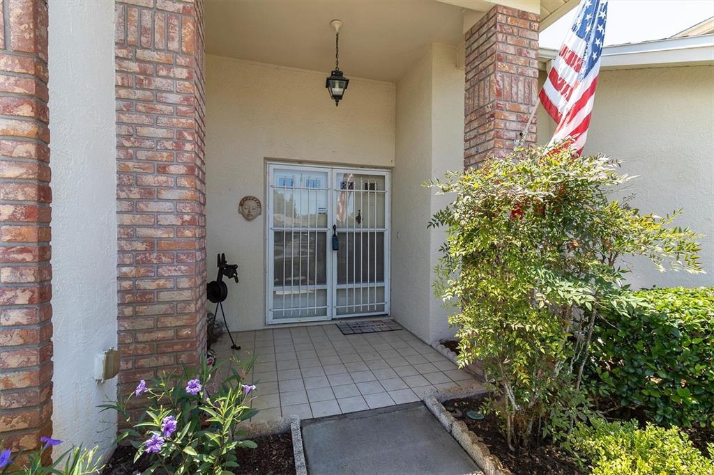 A covered entryway features a tiled porch, brick columns, and a white security screen door — 9052 ARUNDLE PLACE, NEW PORT RICHEY, FL