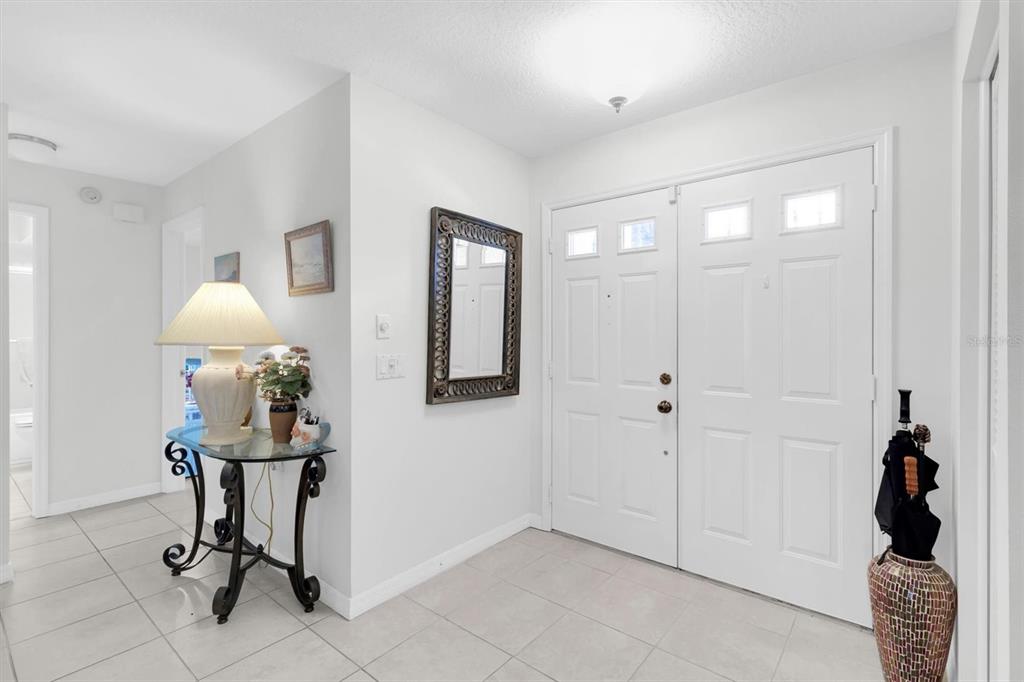 A bright entryway features white double doors, tiled flooring, a glass-topped table, and a mirror — 9052 ARUNDLE PLACE, NEW PORT RICHEY, FL