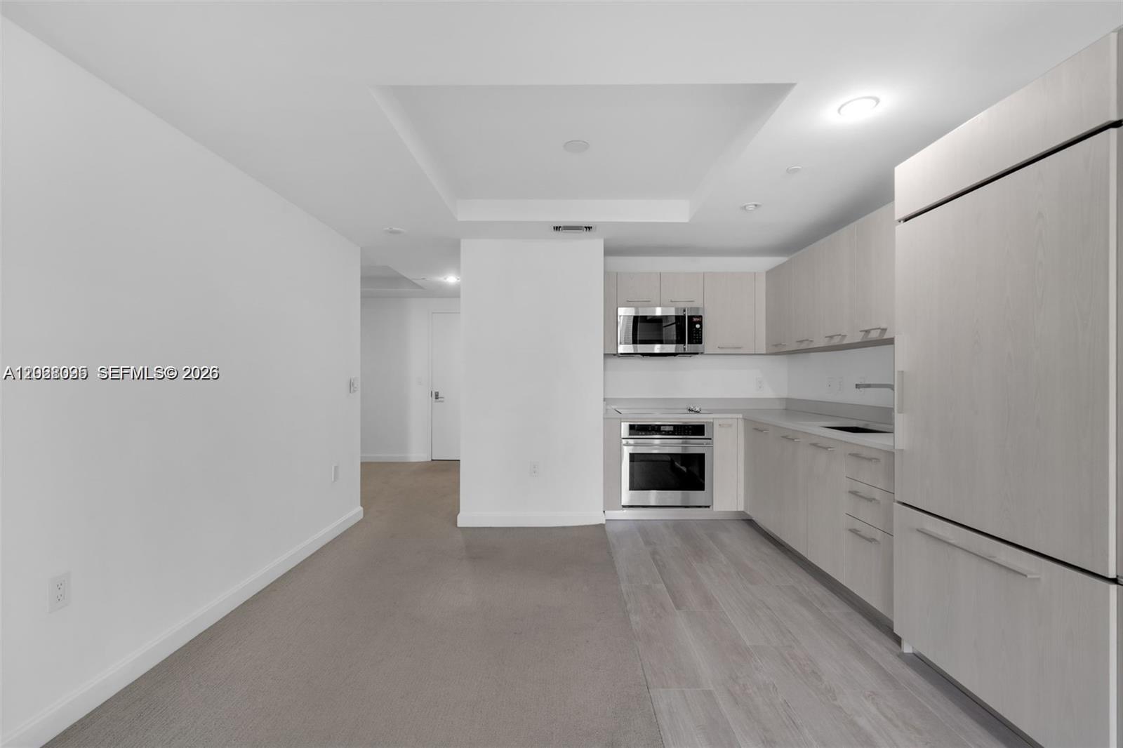 A kitchen with light wood cabinetry and stainless steel appliances sits adjacent to a carpeted area — 45 SW 9th St # 2204, Miami FL 33130, MIAMI, FL