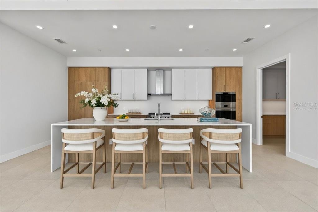 A modern kitchen features a large white island with four stools and wood-accented cabinetry — 275 1ST AVENUE S UNIT 4202, ST PETERSBURG, FL