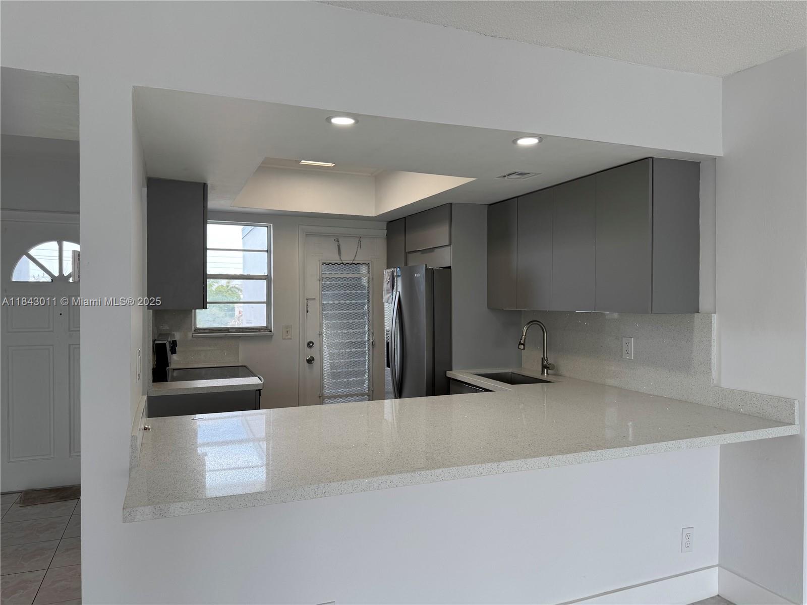 A kitchen features gray cabinets, quartz countertops, a stainless steel refrigerator, and a breakfast bar — 1333 E Hallandale Beach Blvd # 444, Hallandale Beach FL 33009, HALLANDALE BEACH, FL