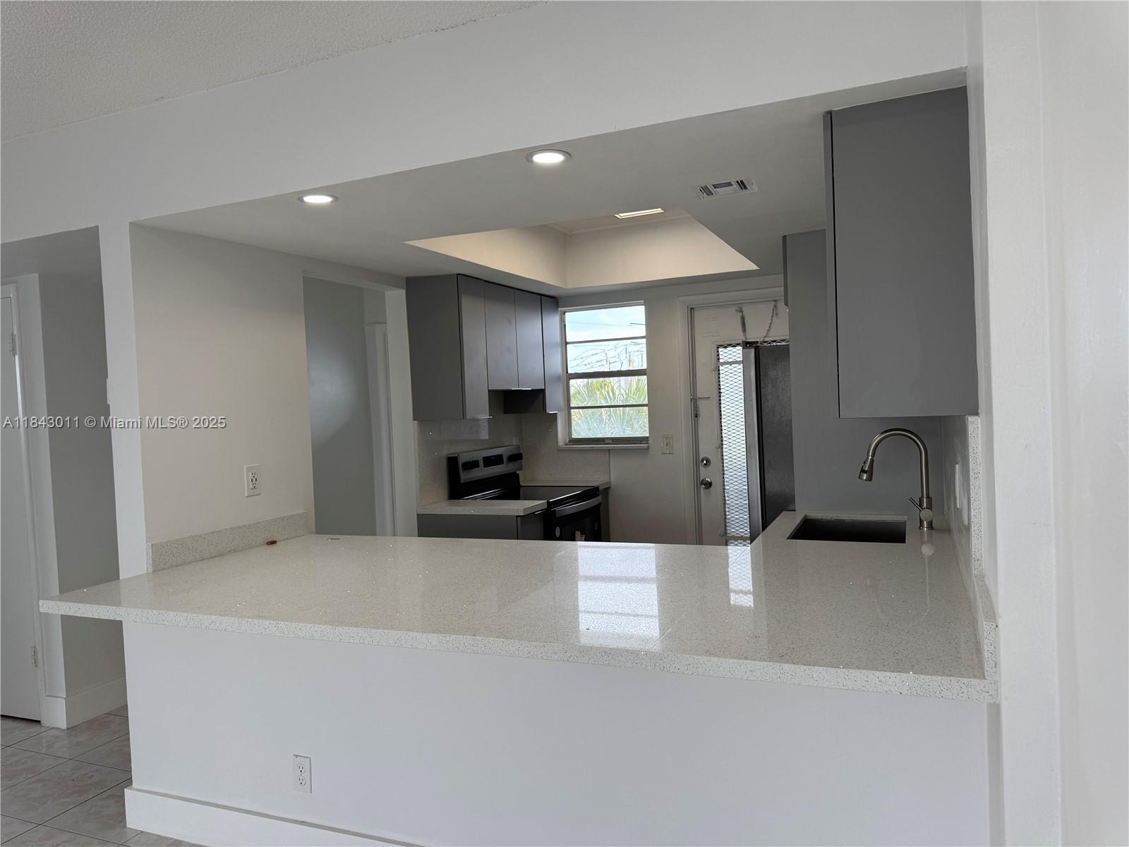 A kitchen features gray cabinets, white quartz countertops, and a breakfast bar — 1333 E Hallandale Beach Blvd # 444, Hallandale Beach FL 33009, HALLANDALE BEACH, FL