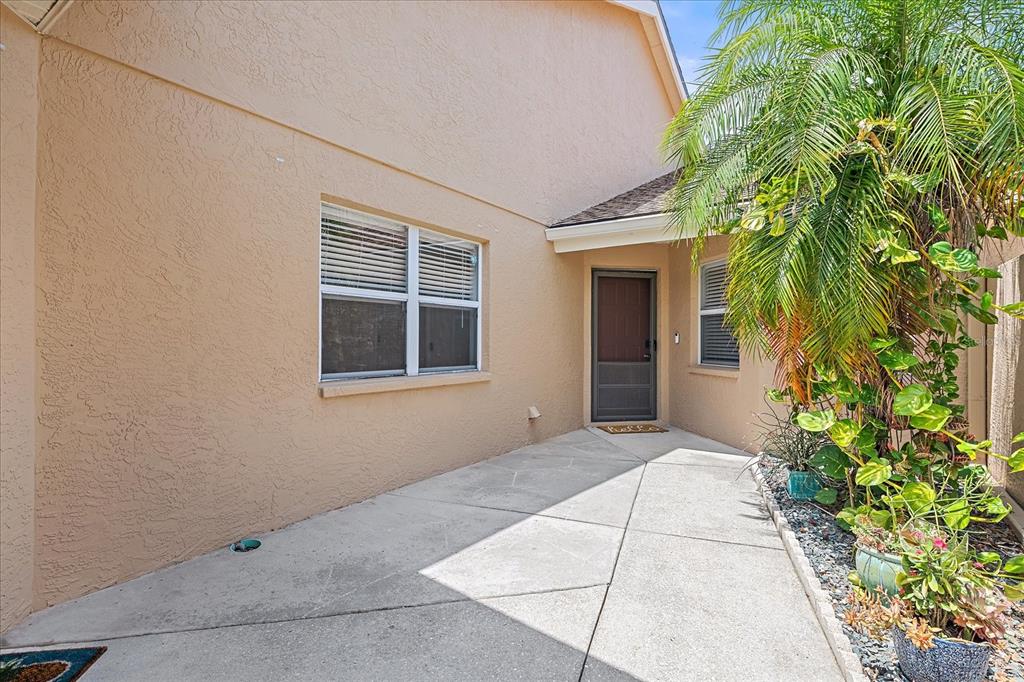 A concrete walkway leads to the front entrance of a tan stucco house with landscaping — 5647 MONTE ROSSO ROAD, SARASOTA, FL