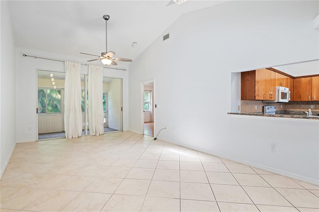A living room with tile flooring, a vaulted ceiling, a ceiling fan, and sliding glass doors — 5647 MONTE ROSSO ROAD, SARASOTA, FL